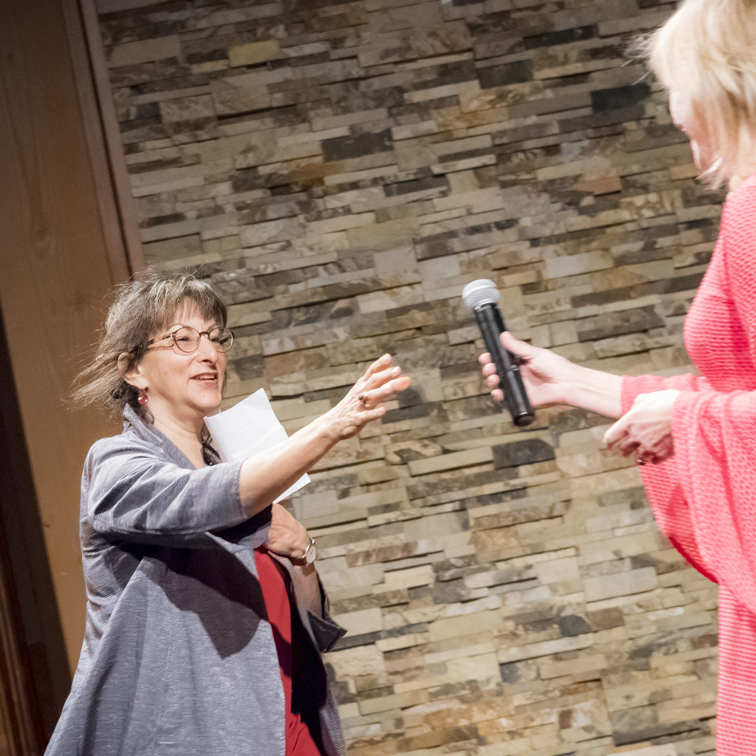 Anita Walker handing the microphone to Maggie Holtzberg.