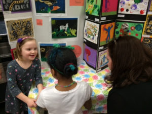 Girls standing in front of their artworks at a Creative Minds Out of School Time exhibition.