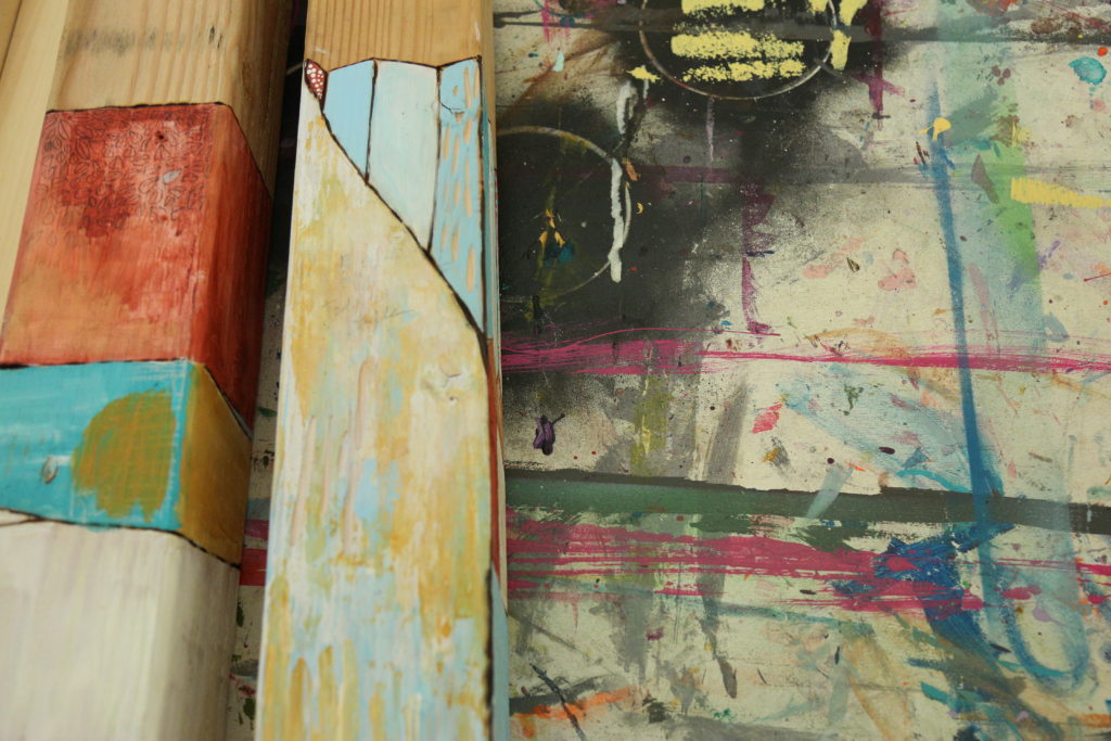 photo of a paint-splotched work surface and some 2 x 2 pieces of wood with different shapes drawn and painted on them.