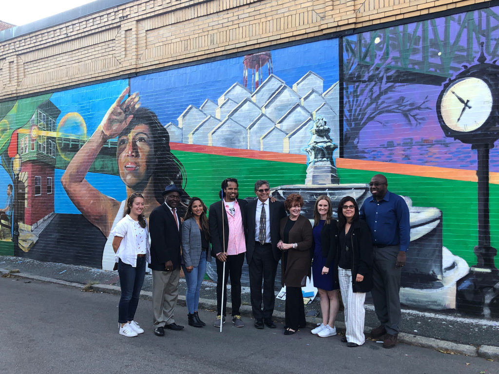 Community members stand in front of the “Chelsea Right Now” mural painted by Demetrius Fuller.