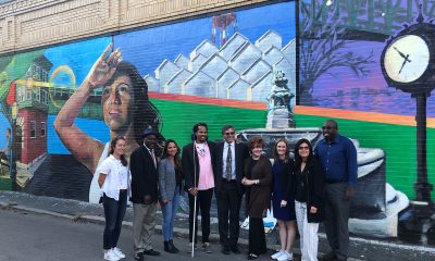 Community members stand in front of a mural