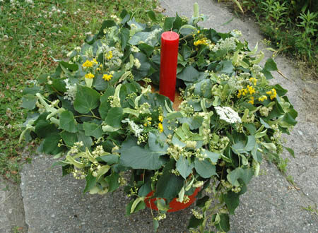 A wreath Jonas made with linden leaves and yellow daisies surrounding a red candle.