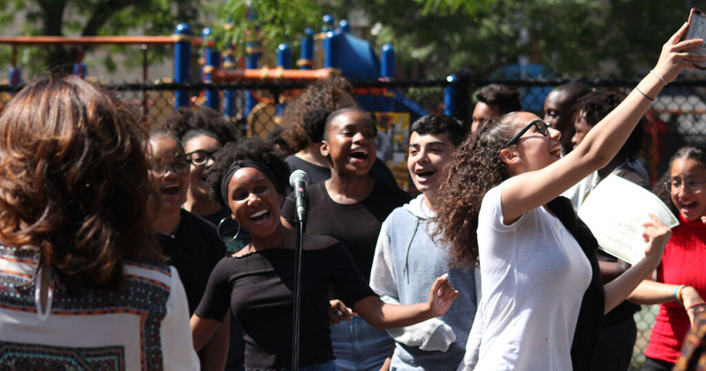 A small group of youth artists singing and smiling during an outdoor performance