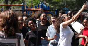 A small group of youth artists singing and smiling during an outdoor performance