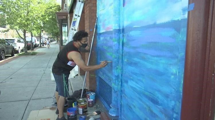 Man with dark, curly hair wears a mask while painting a mural 