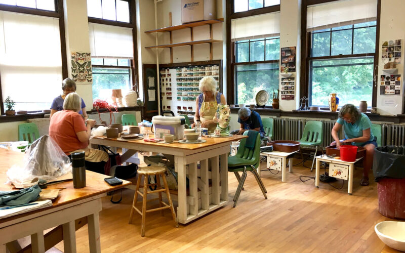 People working around a table and at a potters wheel in a ceramics class at the Munroe Center for the Arts