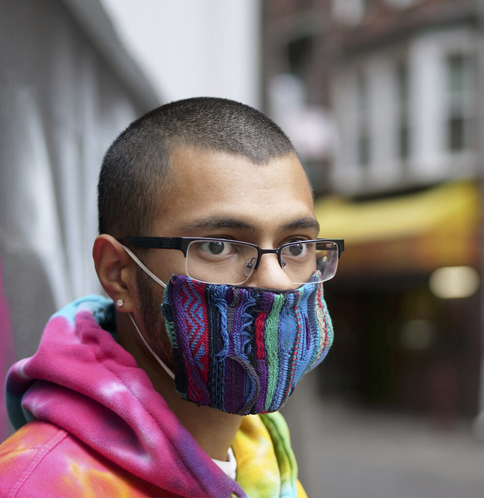 Young man with a buzz cut, glasses, a colorful face mask, wearing a tie-dyed hoodie