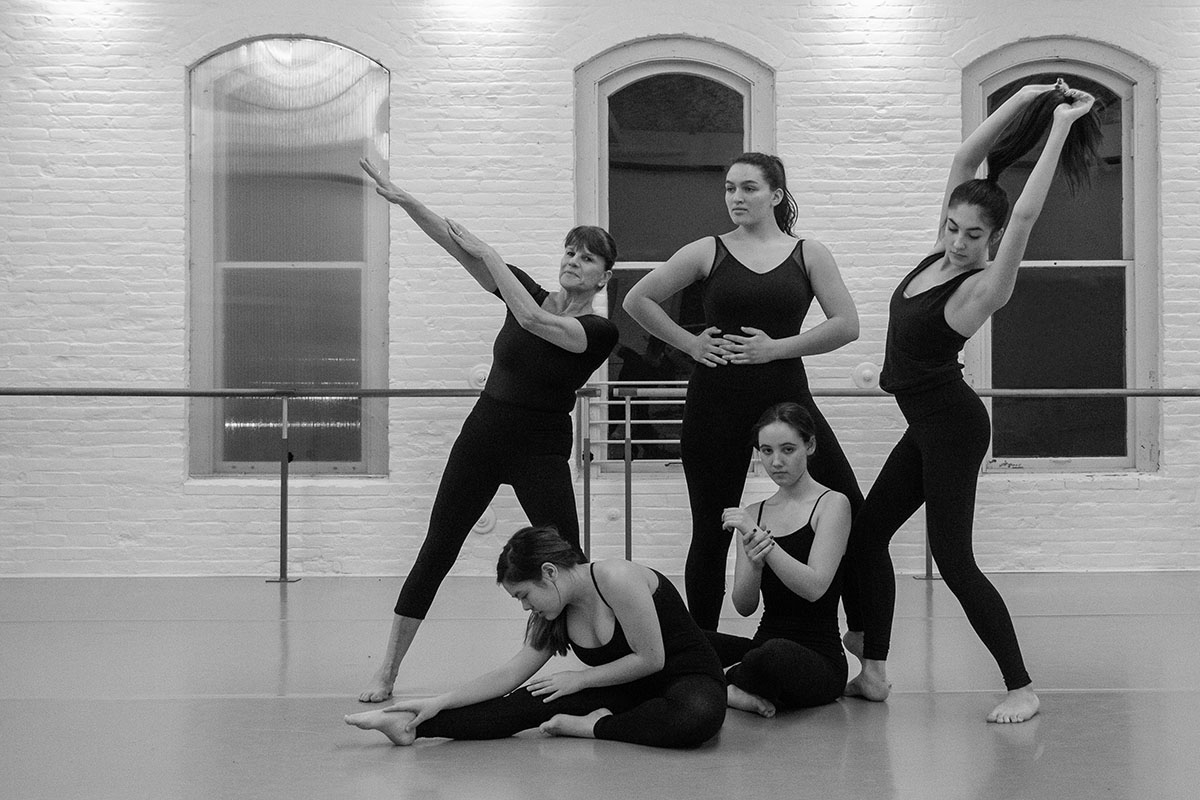 Five dancers in black leotards