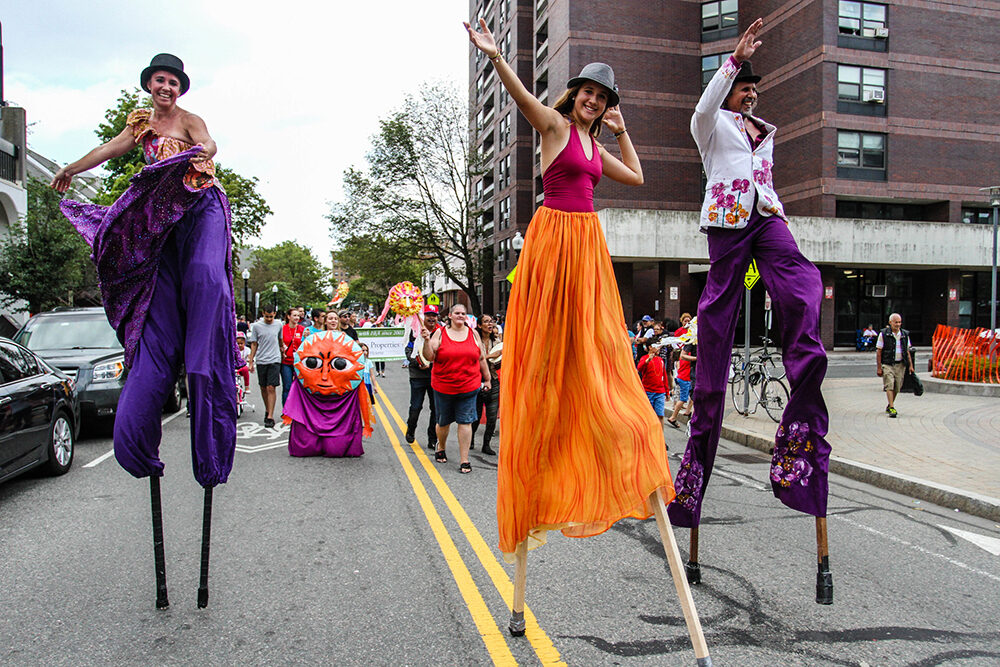 three people walk on stilts, wearing bright, flowing pants as part of IBA's Festival Betances 