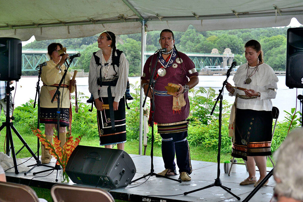 Four performers in Native American dress on a stage sing and play instruments