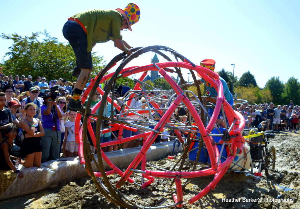 two people working to get their kinetic sculpture through a patch of mud during the Lowell Kinetic Sculpture Race