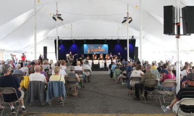 Under a large, white tent audience members sit in folding chairs watch a jazz music performance.