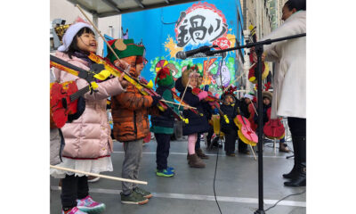 Children wearing winter hats and coats playing stringed instruments while performing outside.