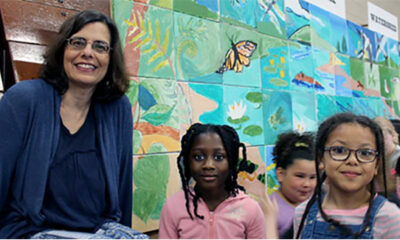 A woman and two children stand in front of a mural they made at May Street School