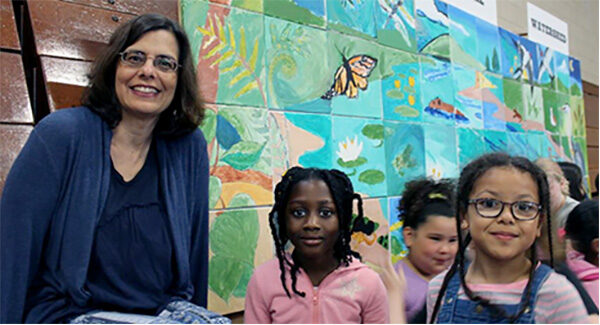 A woman and two children stand in front of a mural they made at May Street School