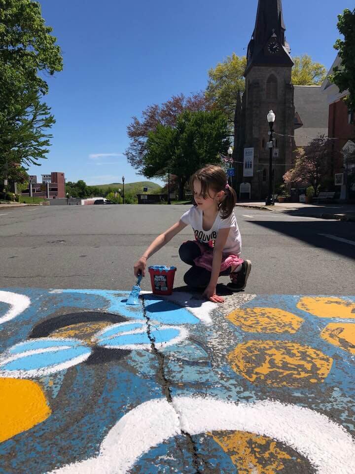 Girl painting a mural outside under a bright blue sky