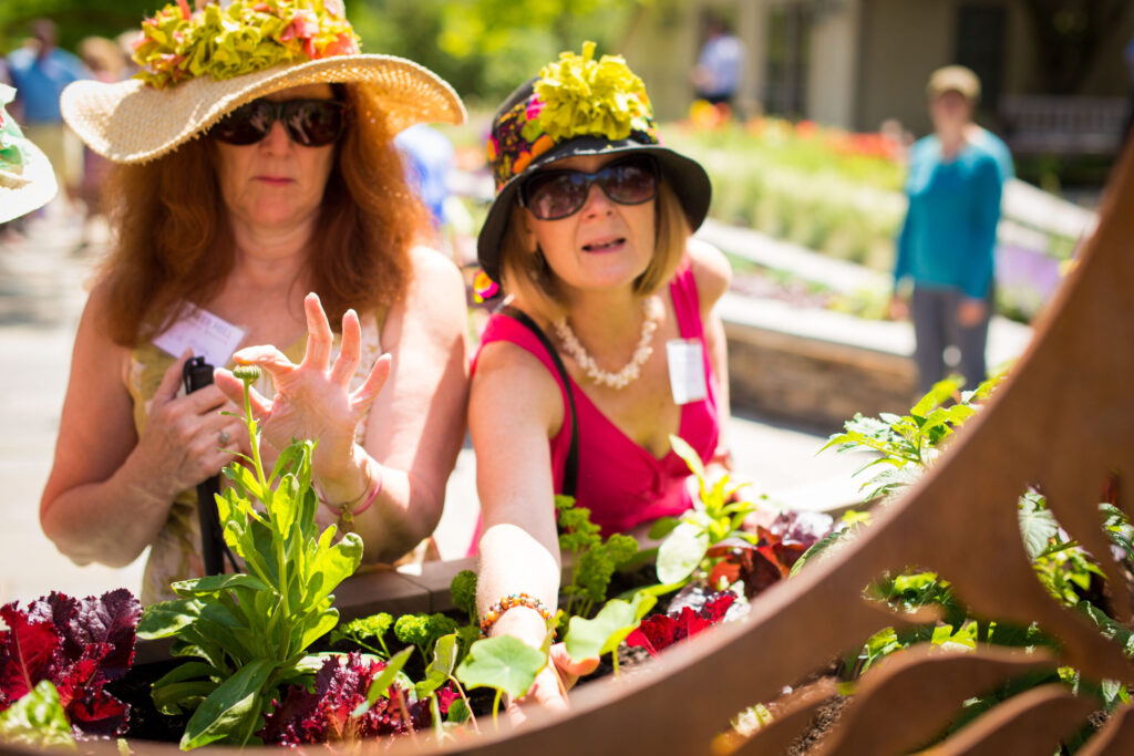 two women in floppy, floral hats and sunglasses touching plants in the Garden within Reach