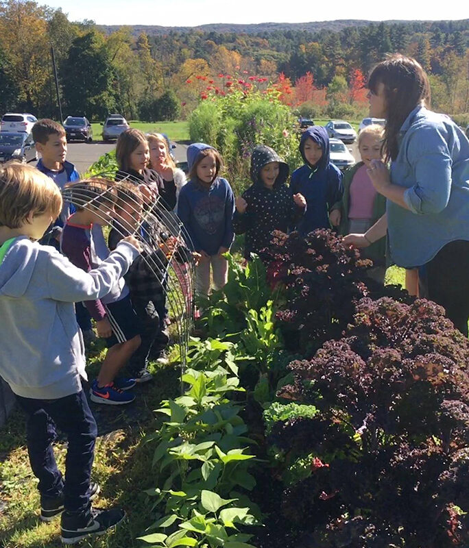 10 students stand in front of a row of cabbages and kale, mountains and fall foliage in the background