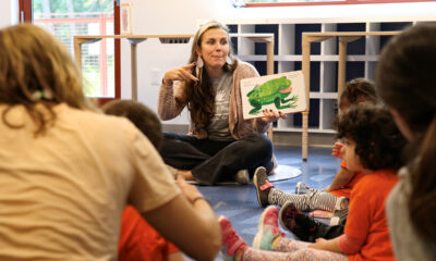 Woman sitting cross-legged on the floor signs a book by Eric Carle to a group of children seated on the floor around her