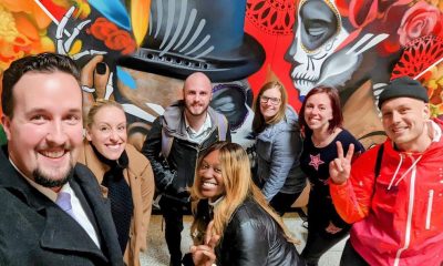 7 smiling people standing in front of a mural
