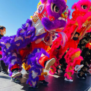 Young people wearing traditional dragon costumes - one is pink, the other purple - as part of a May Day celebration