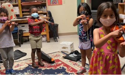 4 students wearing masks and holding their violins in a music classroom