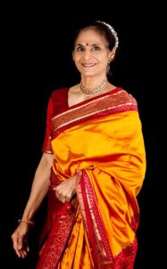 a woman with dark hair pulled back and a bindi wears a richly colored sari of reds and golds