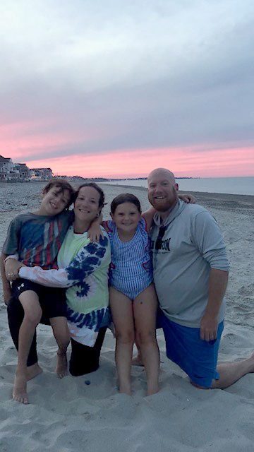 photo of two parents and their 2 children on a beach at twilight, their arms all entwined