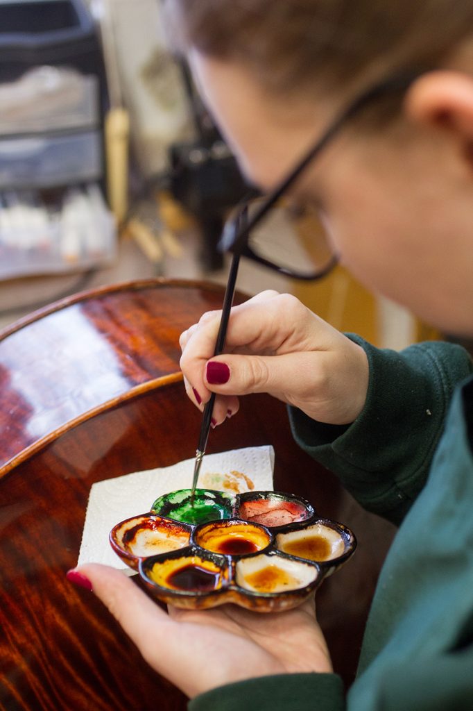 photo of person doing touch up painting on a stringed instrument. Photo: Cydney Scott Photography.
