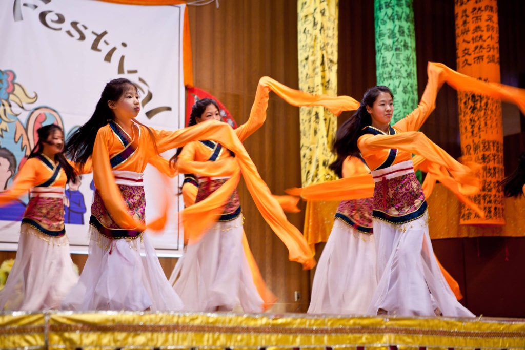 photo of 6 young people performing a traditional dance, long sleeves of cloth floating around as they move