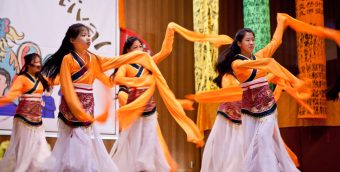 photo of 6 young people performing a traditional dance, long sleeves of cloth floating around as they move