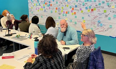 photo of staff and board members sitting at a long table, a wall of post-its hanging behind them from a strategic planning exercise