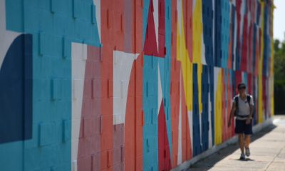 photo of a person walking along a building that has a brightly-colored geometric mural painted on it