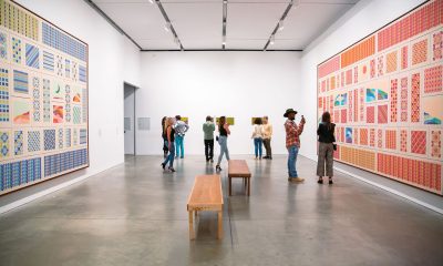 photo of a gallery at the Institute of Contemporary Art - a handful of visitors standing in the back ground, a wooden bench cuts through into the foreground. Large canvases hang of walls to teh left anf right side of the frame