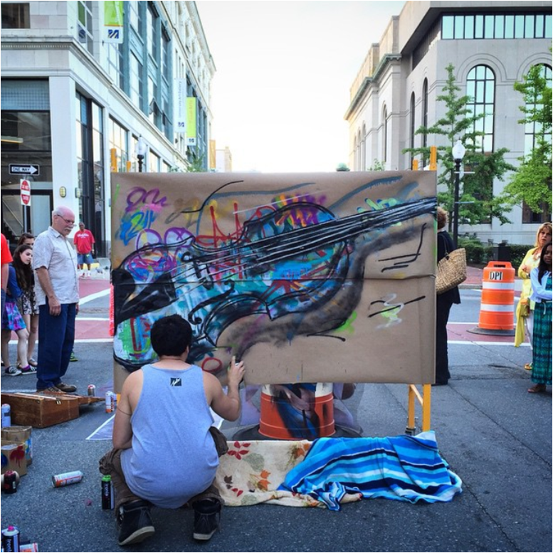 photo of an artist crouching in the street painting a canvas using spray cans