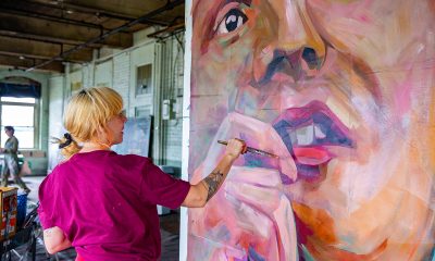 photo of a painter holding a brush, working on a large painting of a person's face