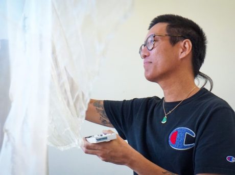 photo of a man with glasses and buzzed hair installing a piece of sheer fiber art