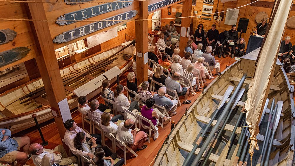 Overhead view of people in row seating at the Shipwreck and Lifesaving Museum, large historic boats on display on either side of them.