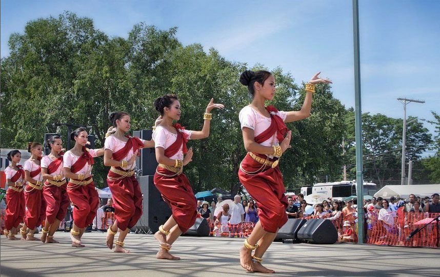 7 dancers wearing traditional Cambodian attire perform in a line on an outdoor stage