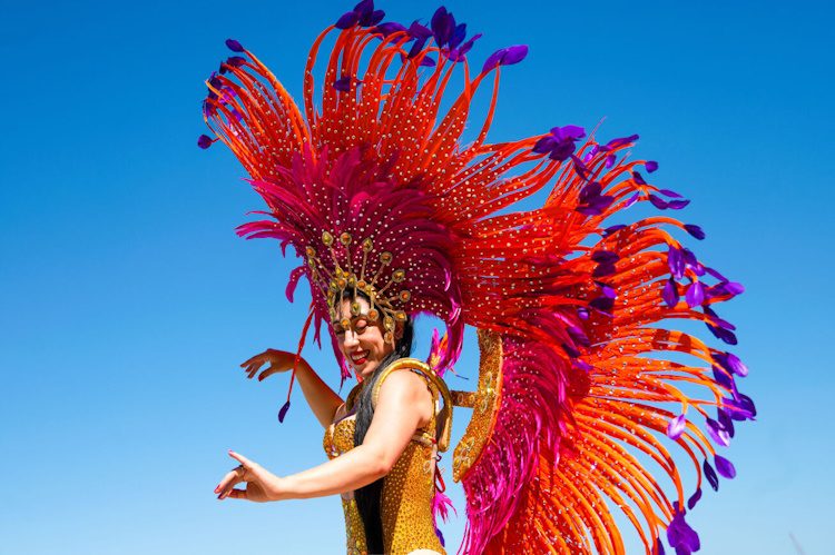 Photo of a Latina woman dancing, wearing a dazzling feathered headpiece and a golden dancewear.