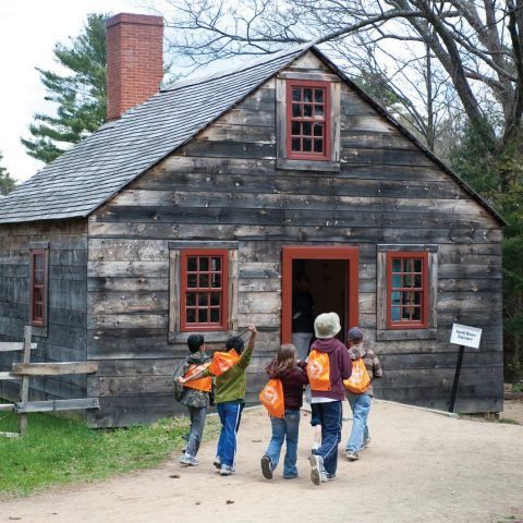 a group of kids walking towards one of the historic buildings in Old Sturbridge Village