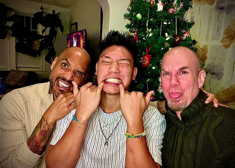 photo of 3 men making silly faces in front of their Christmas tree