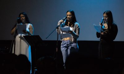 3 young people standing at microphones on a dramatically lit stage performing at a spoken word event