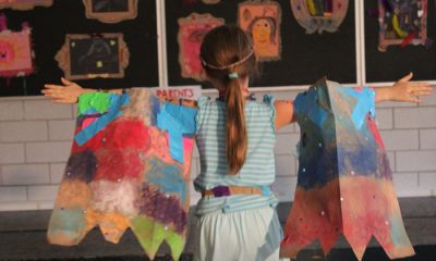 photo of a child facing away from the camera with outstretched arms, both of which have colorfully painted panels hanging from them