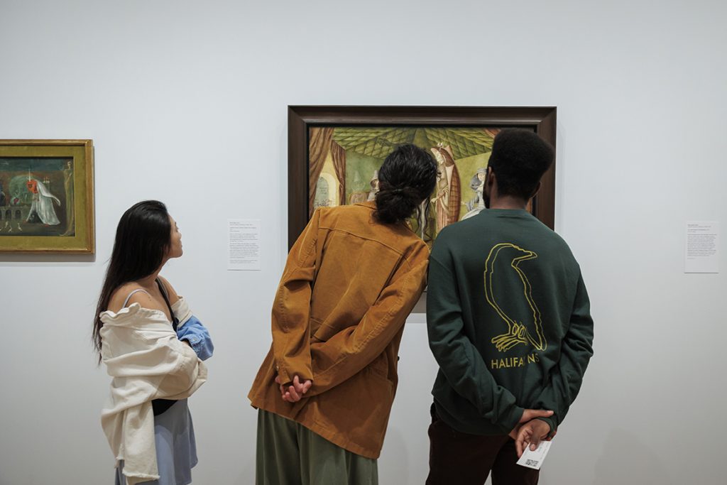 photo of the backs of 3 museum-goers heads, only sections of the painting they are looking are visible in the background 