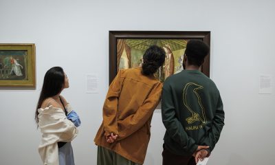 photo of the backs of 3 museum-goers heads, only sections of the painting they are looking are visible in the background