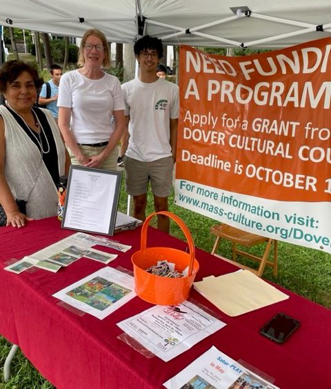 photo of 3 people standing under a tent tabling at a community event. the table in front of them has brochures and the banner behind them has the text: Need funding for a program? Apply for a grant from Dover Cultural Council. 