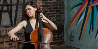 photo of a cello player in a black dress playing in front of a brick wall