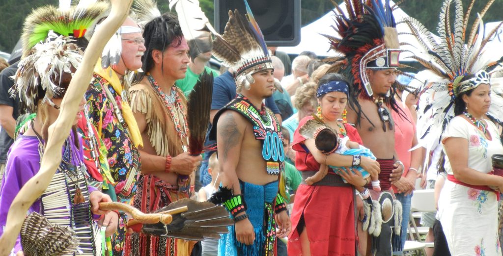 photo of a group of Native Americans dressed in traditional clothing standing together at a Pow Wow