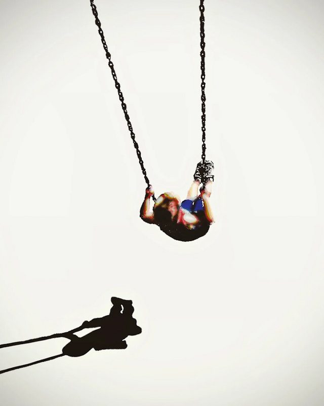 A spare watercolor painting of a child on a swing, casting a shadow over a pale, monochromatic background.